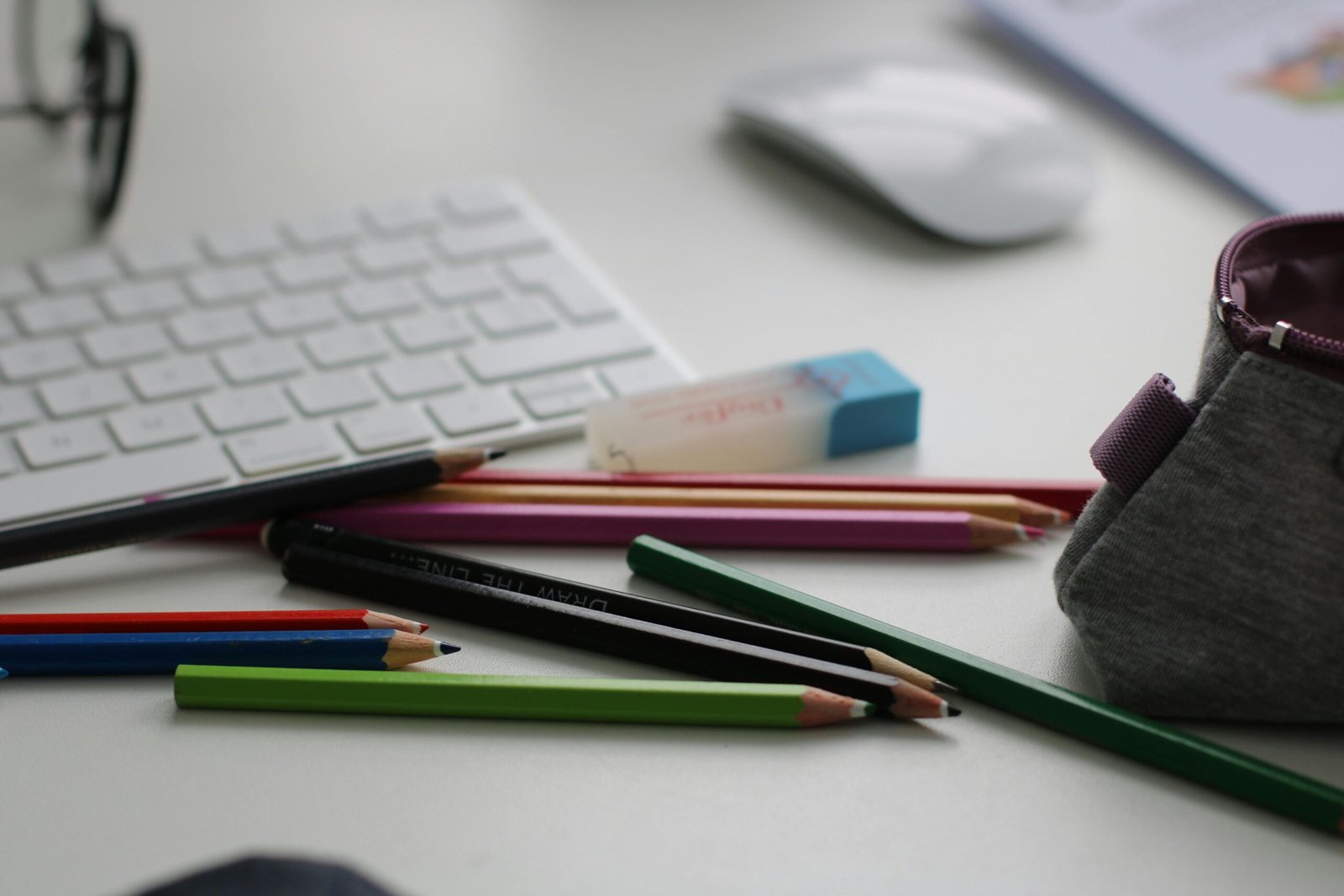 Color pencils and office supplies scattered on a white desk with keyboard and mouse.